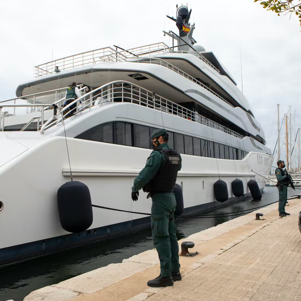 A large white yacht is docked by a dock in Spain as two armed civil guards stand watch
